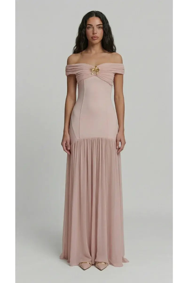 Woman wearing a pink off-shoulder gown with a brooch detail on a light gray background