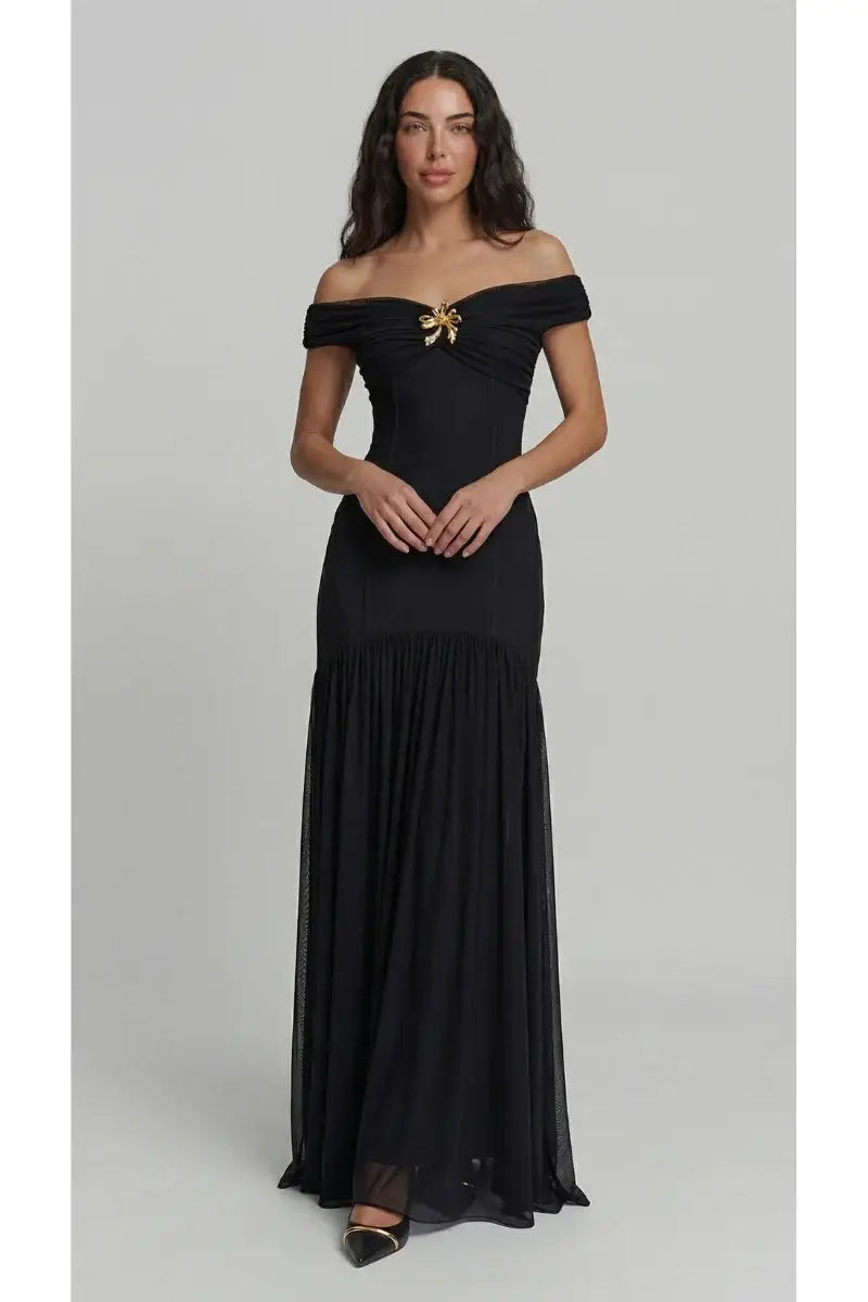 Woman wearing a black off-shoulder gown with a gold bow on a gray background