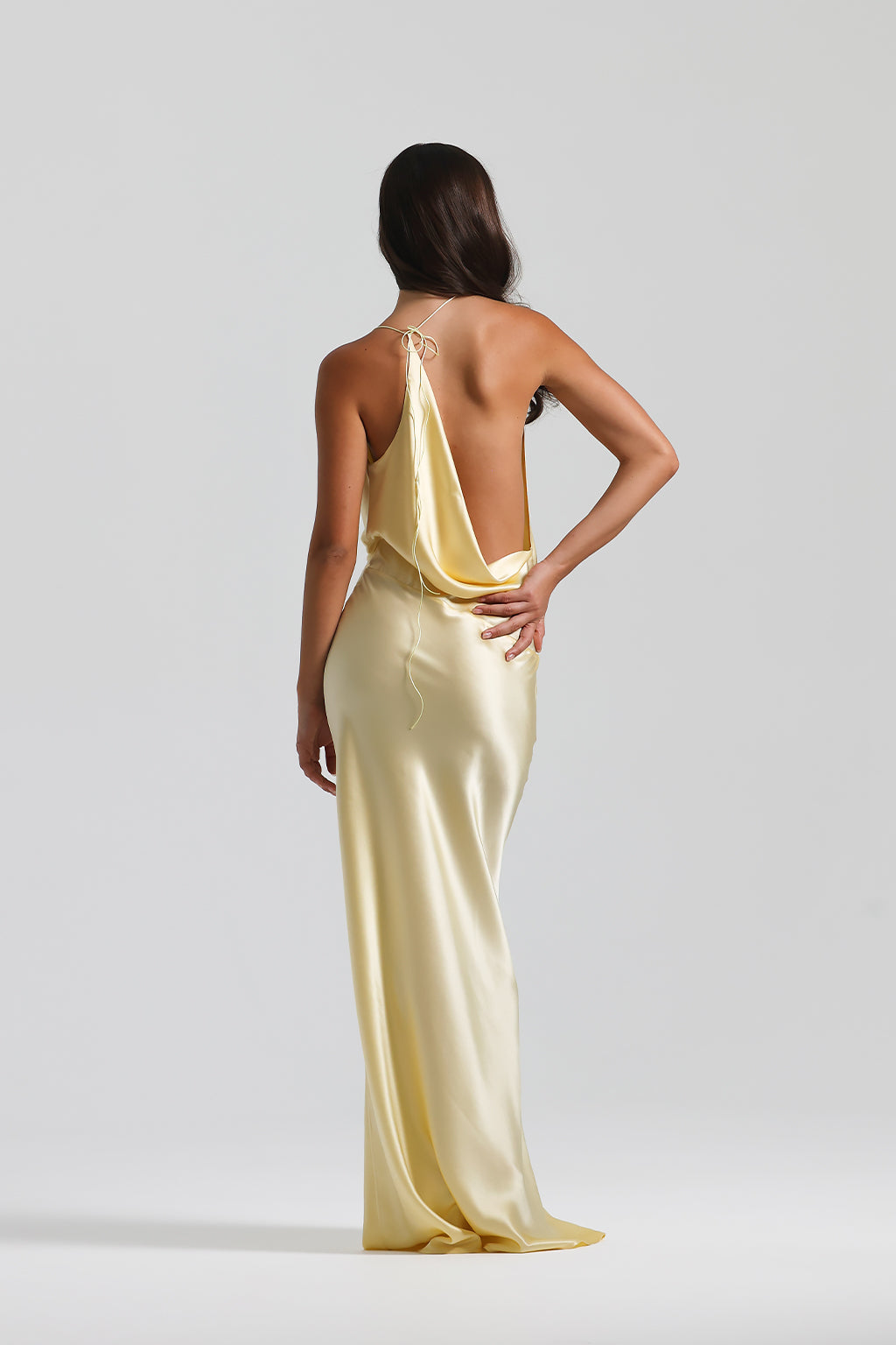 Woman wearing a yellow evening gown with a backless design on a light gray background