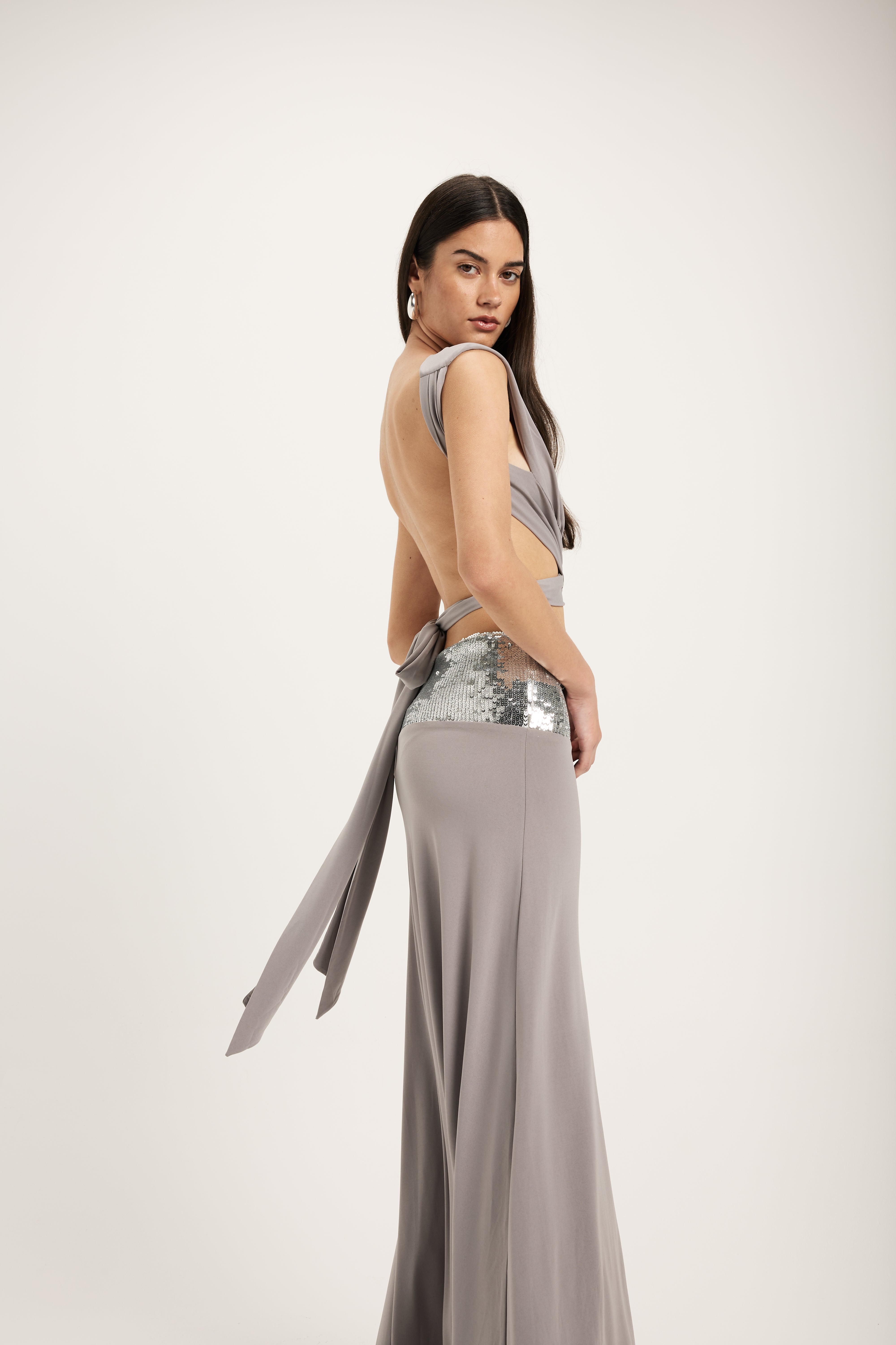 Woman wearing a long, light gray dress with a sequined waistband on a white background