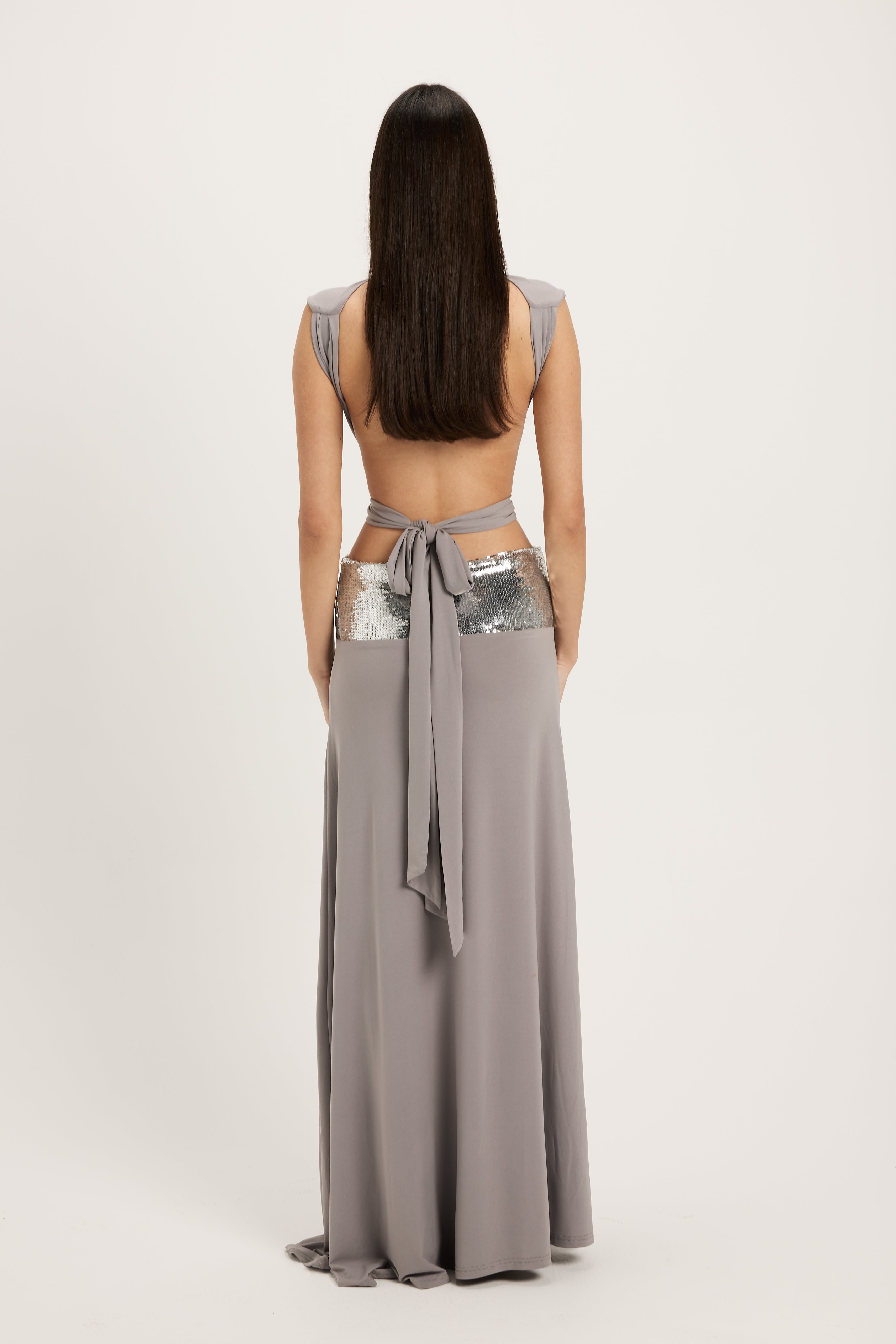 Woman wearing a long gray dress with cut-out sides on a white background