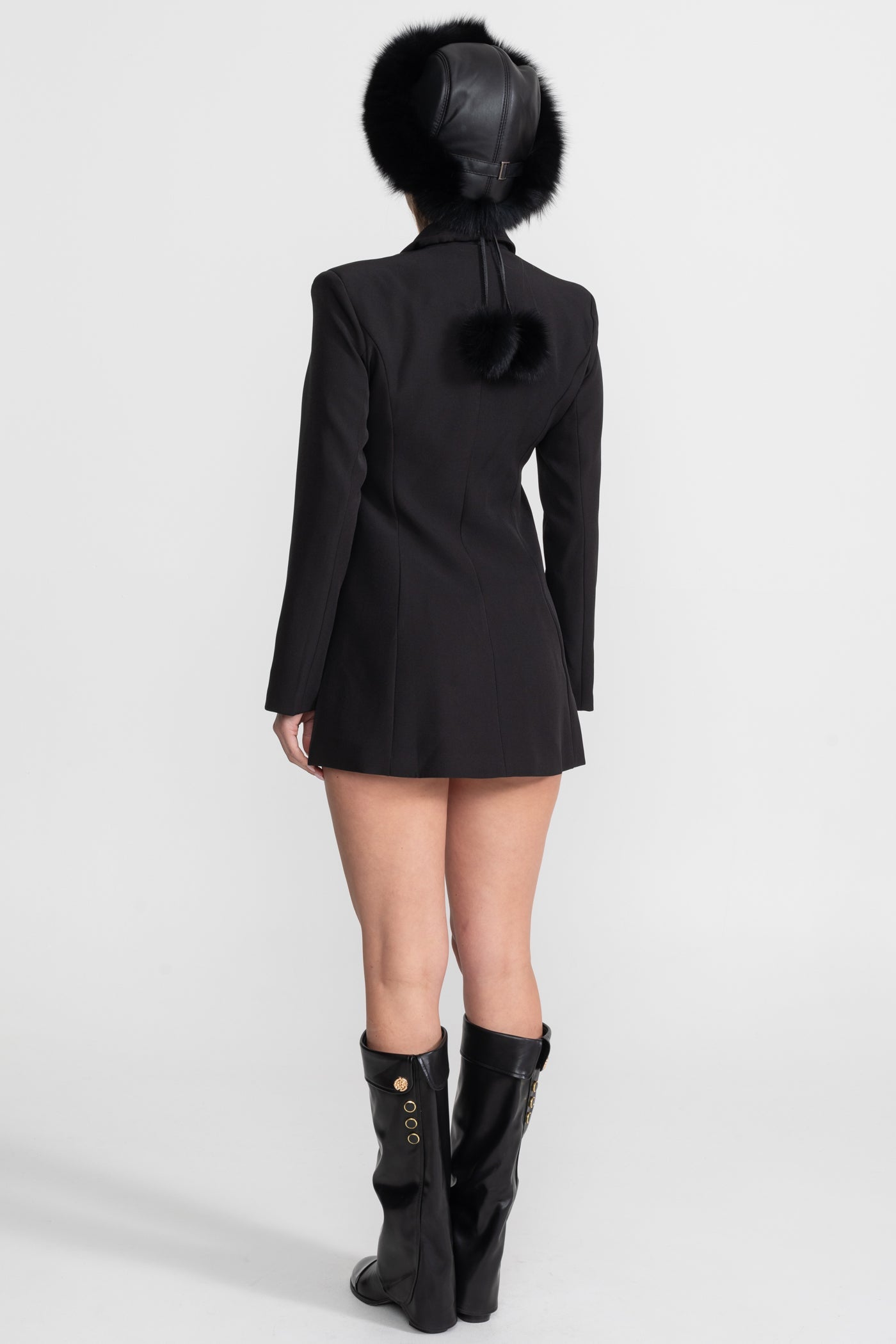 Person wearing a black coat with fur trim and black boots on a white background