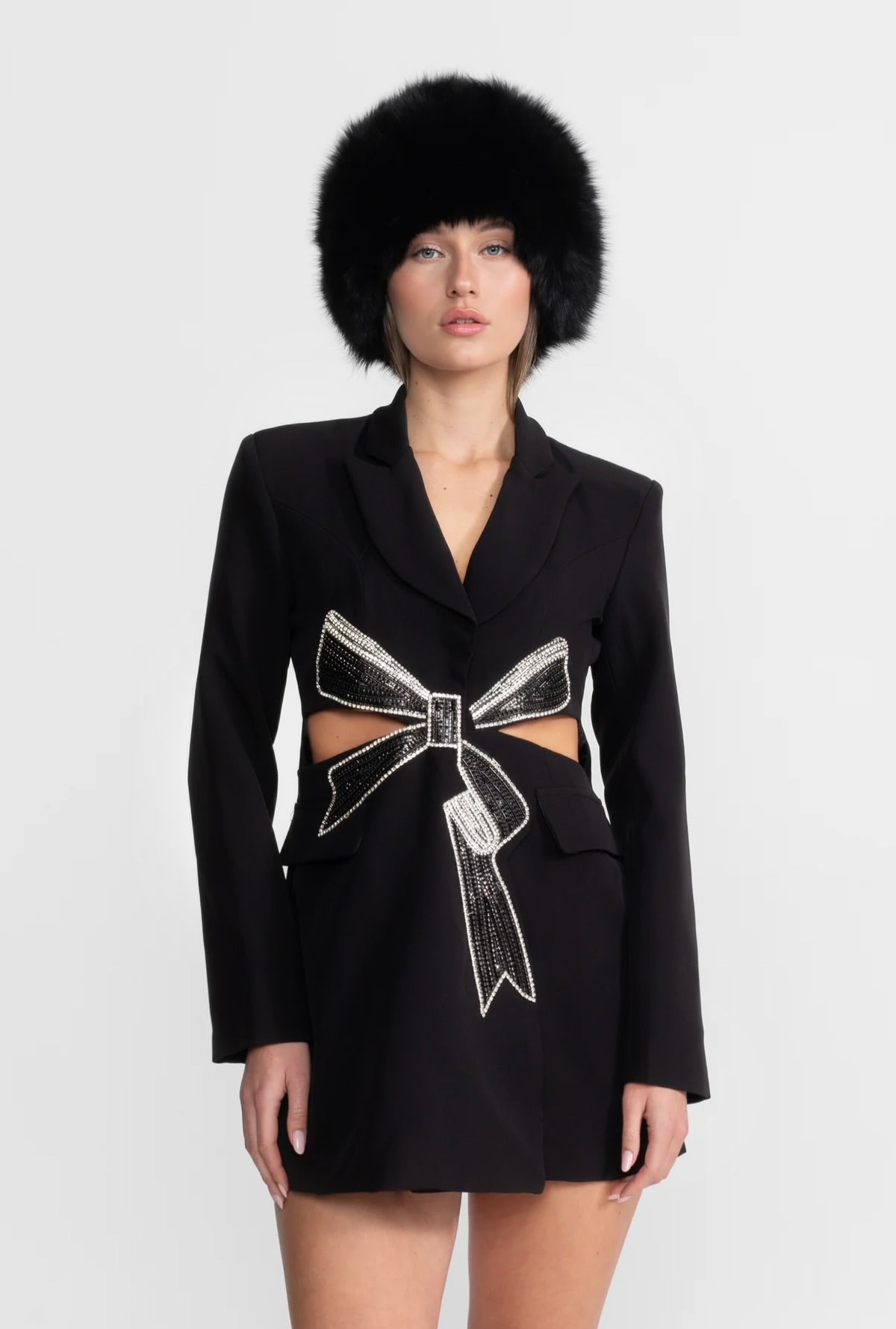 Black blazer dress with cut-out bow design and fur hat on a white background
