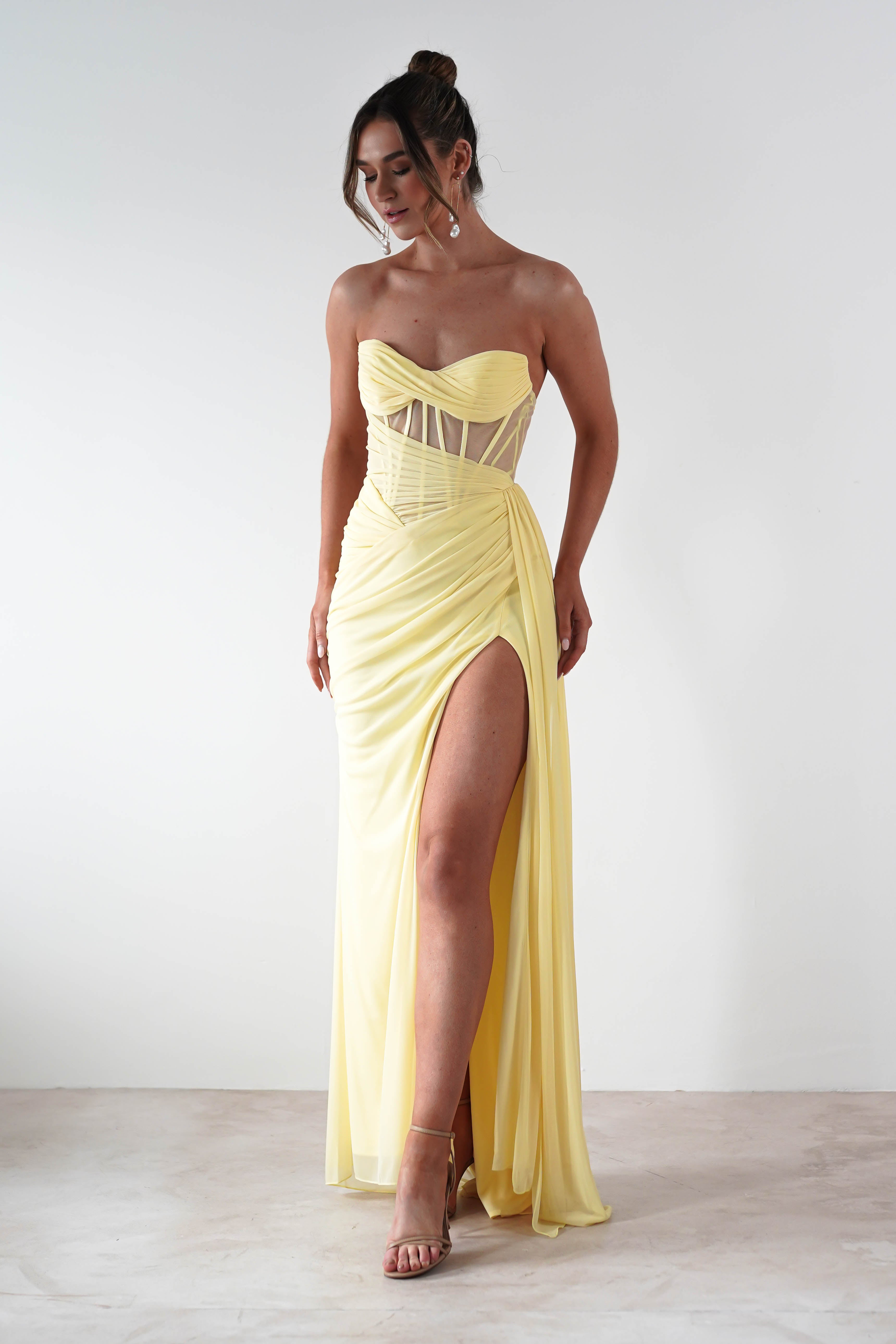 Woman wearing a yellow strapless gown with a high slit on a white background