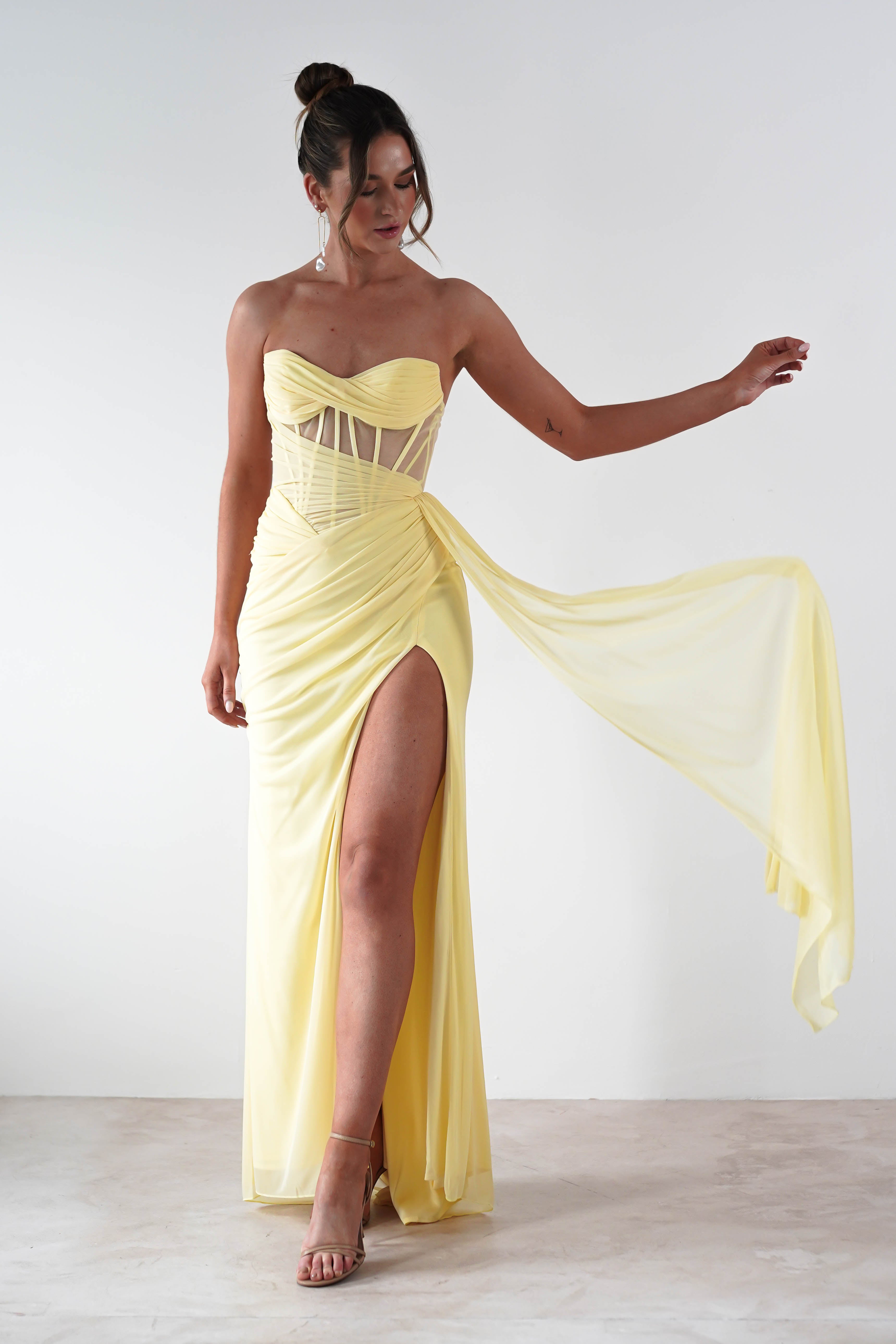 Woman wearing a yellow strapless gown with a slit on a white background