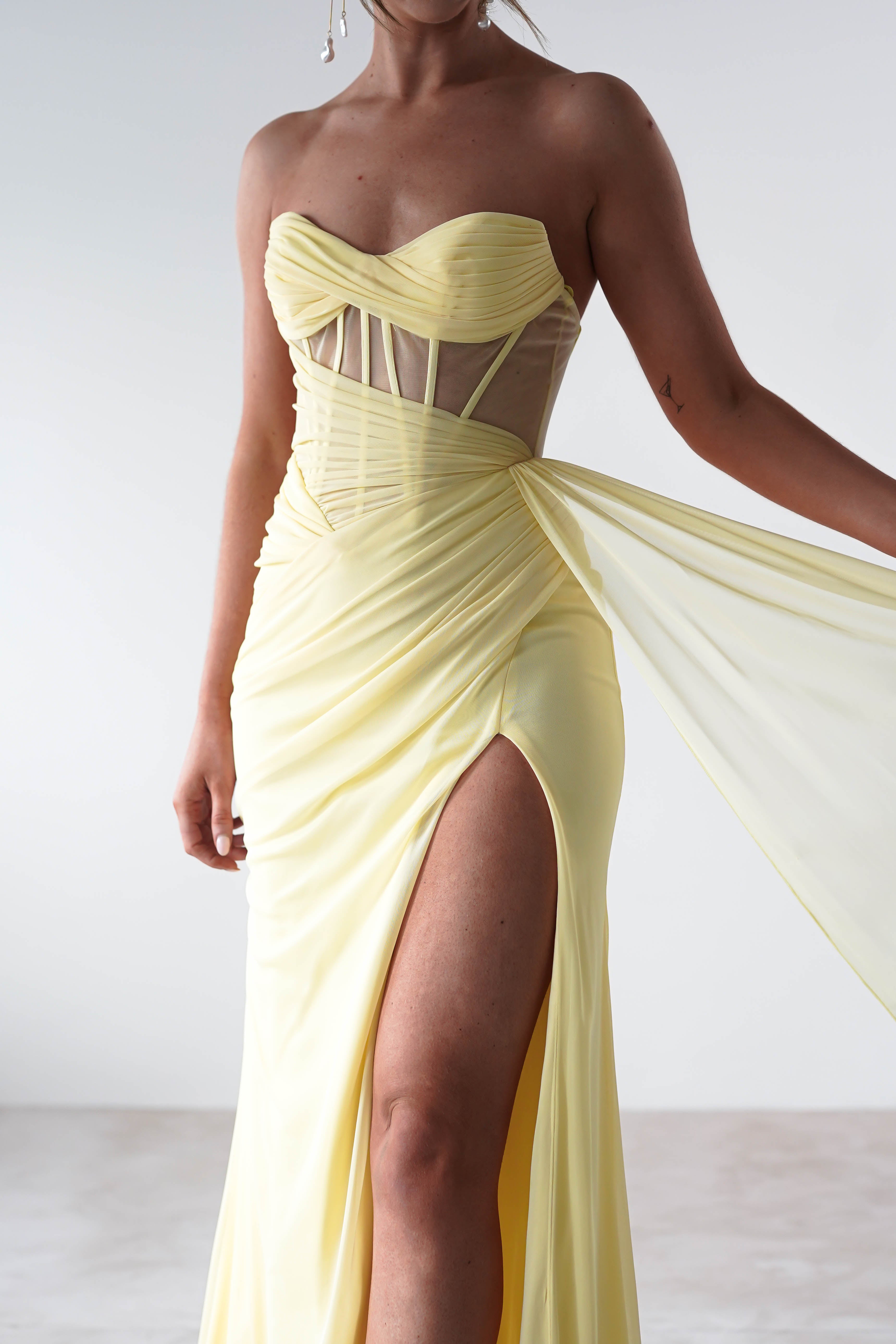Yellow strapless gown with a high slit on a plain background