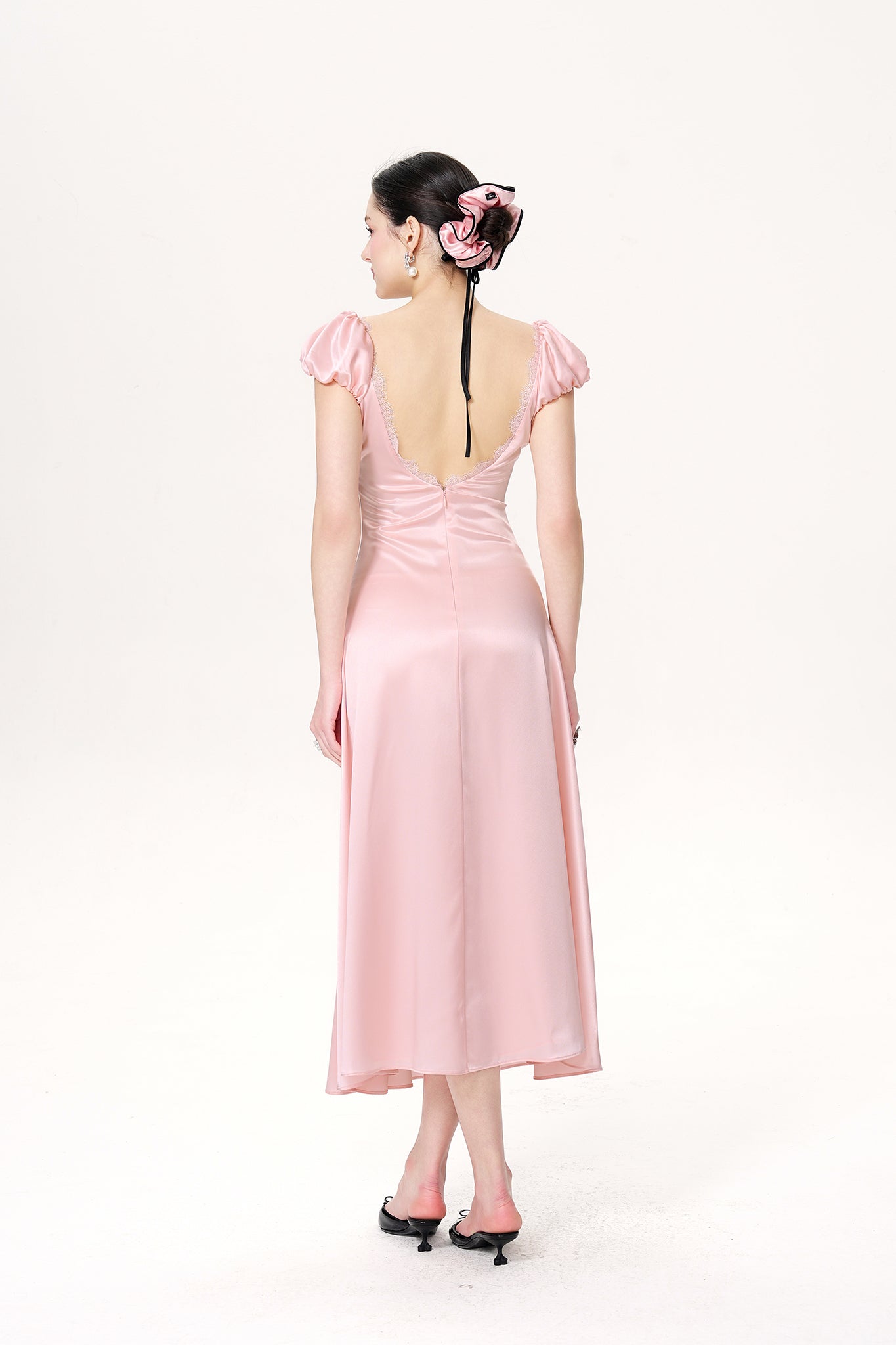 Woman wearing a pink dress with a backless design on a white background