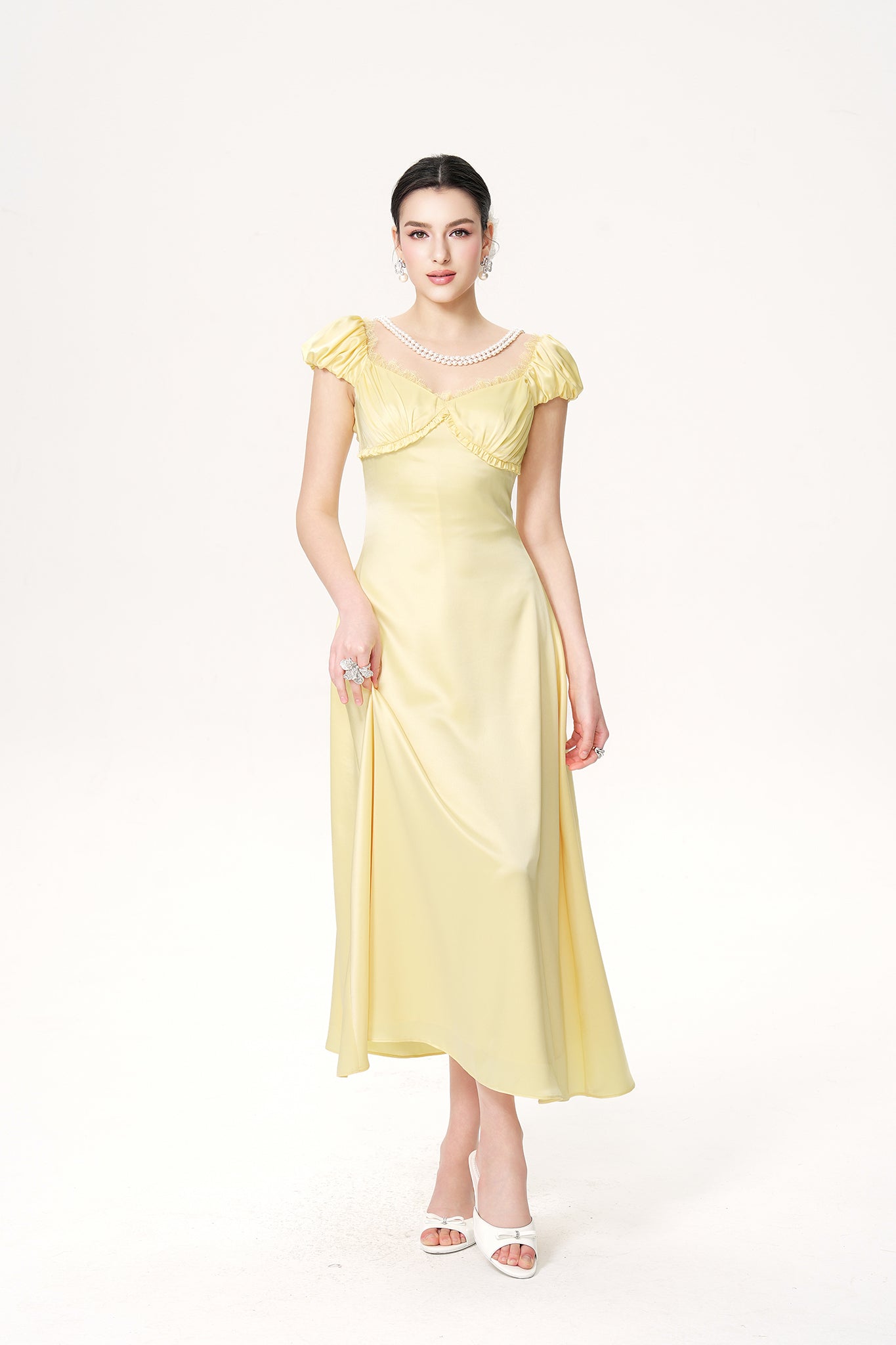 Woman wearing a light yellow dress with ruffled sleeves on a white background