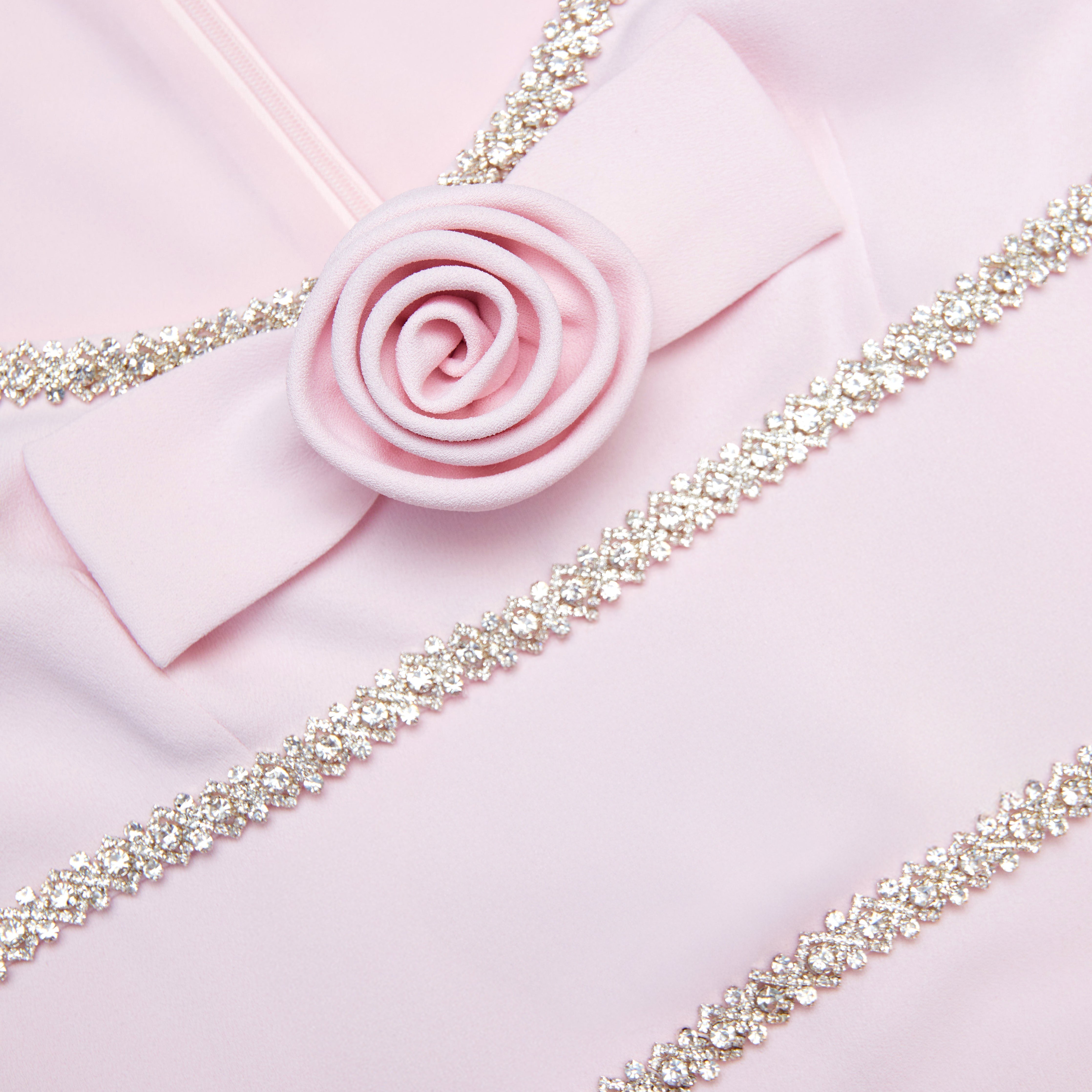 Pink fabric with a decorative rose and sparkling trim on a pink background