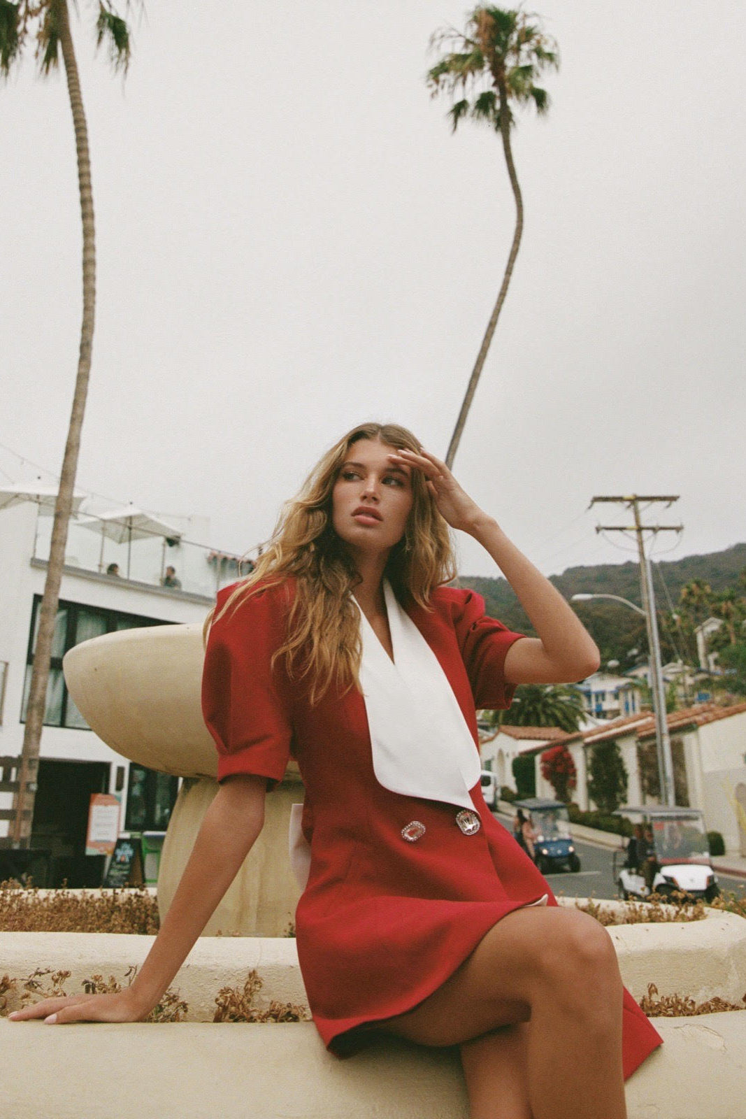 Woman in a red outfit sitting on a bench with palm trees in the background
