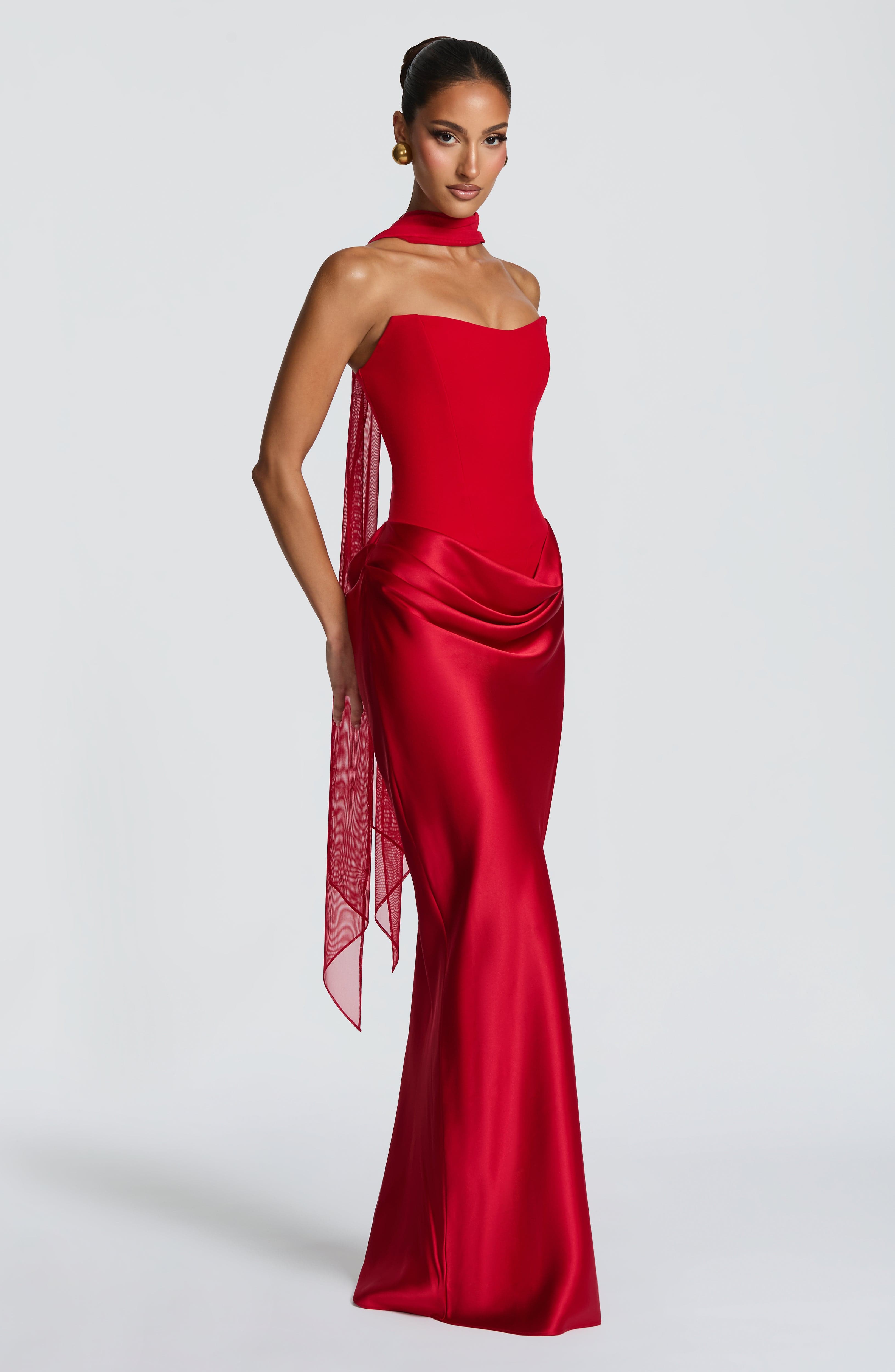 Woman wearing a red evening gown with a sheer overlay on a white background