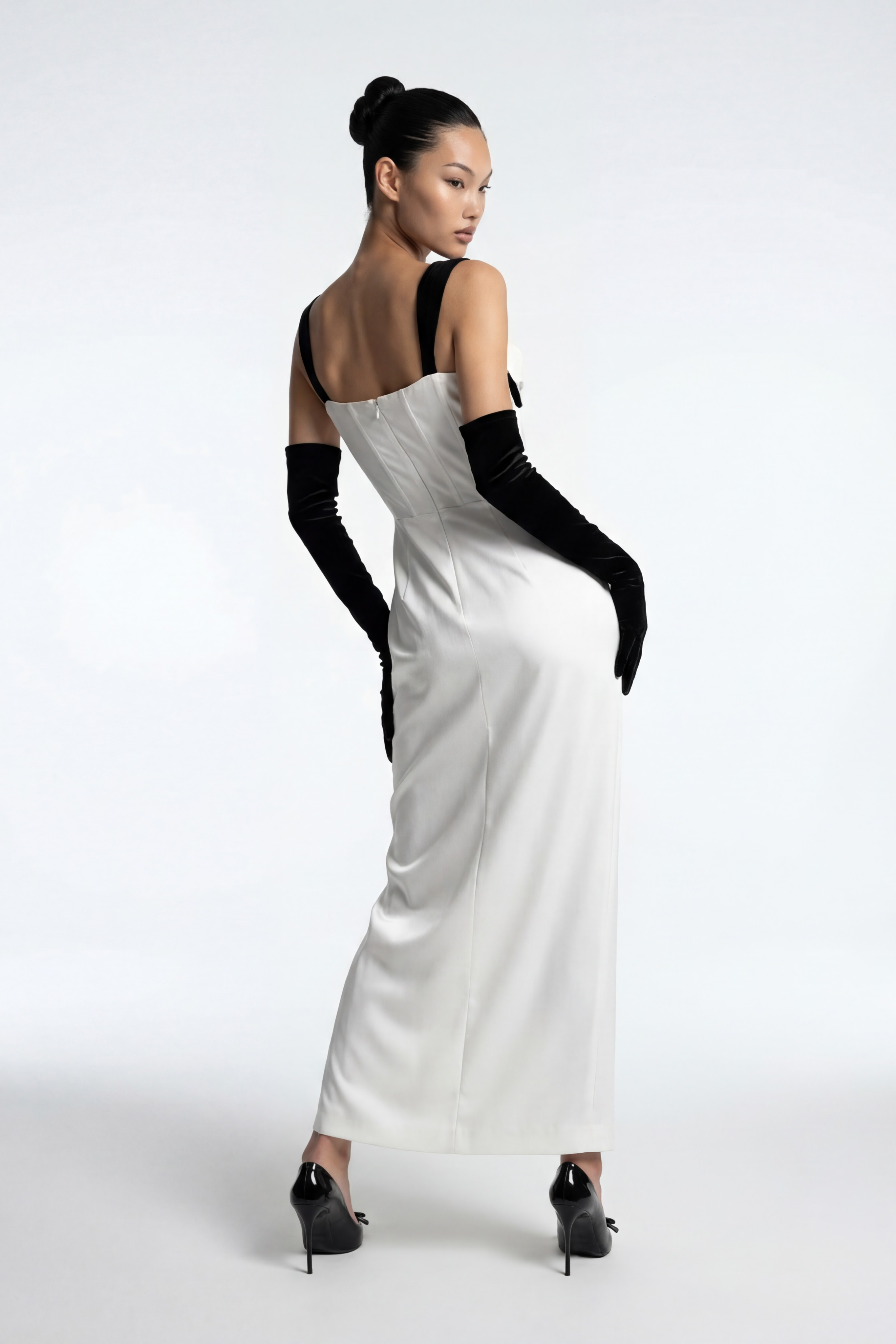 Woman wearing a white evening gown with black gloves on a white background