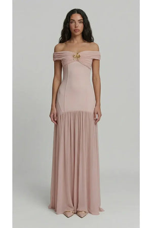 Woman wearing a pink off-shoulder gown with a brooch detail on a light gray background