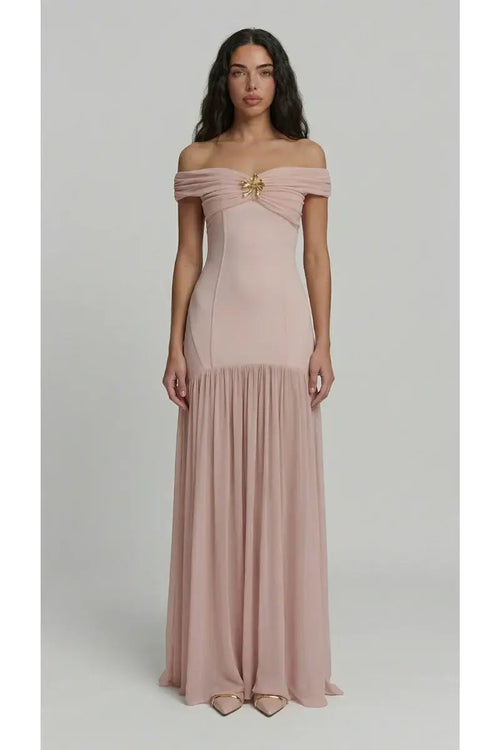 Woman wearing a pink off-shoulder gown with a brooch detail on a light gray background