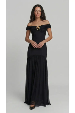 Woman wearing a black off-shoulder gown with a gold bow on a gray background