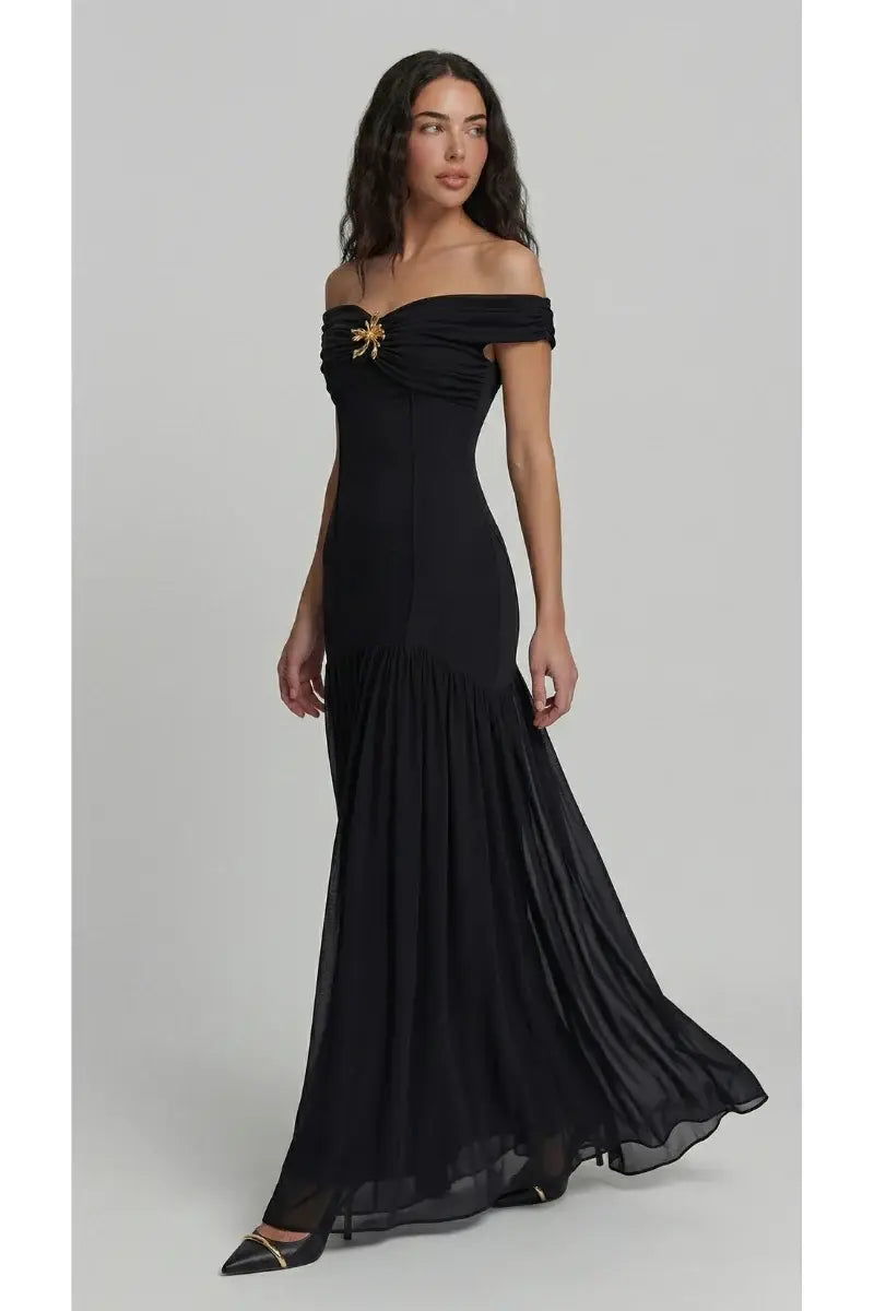 Woman wearing a black off-shoulder gown with gold accents on a gray background