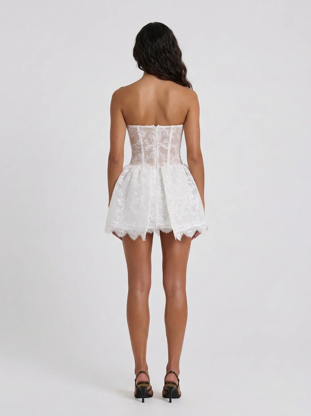 Woman wearing a white lace strapless dress on a plain background
