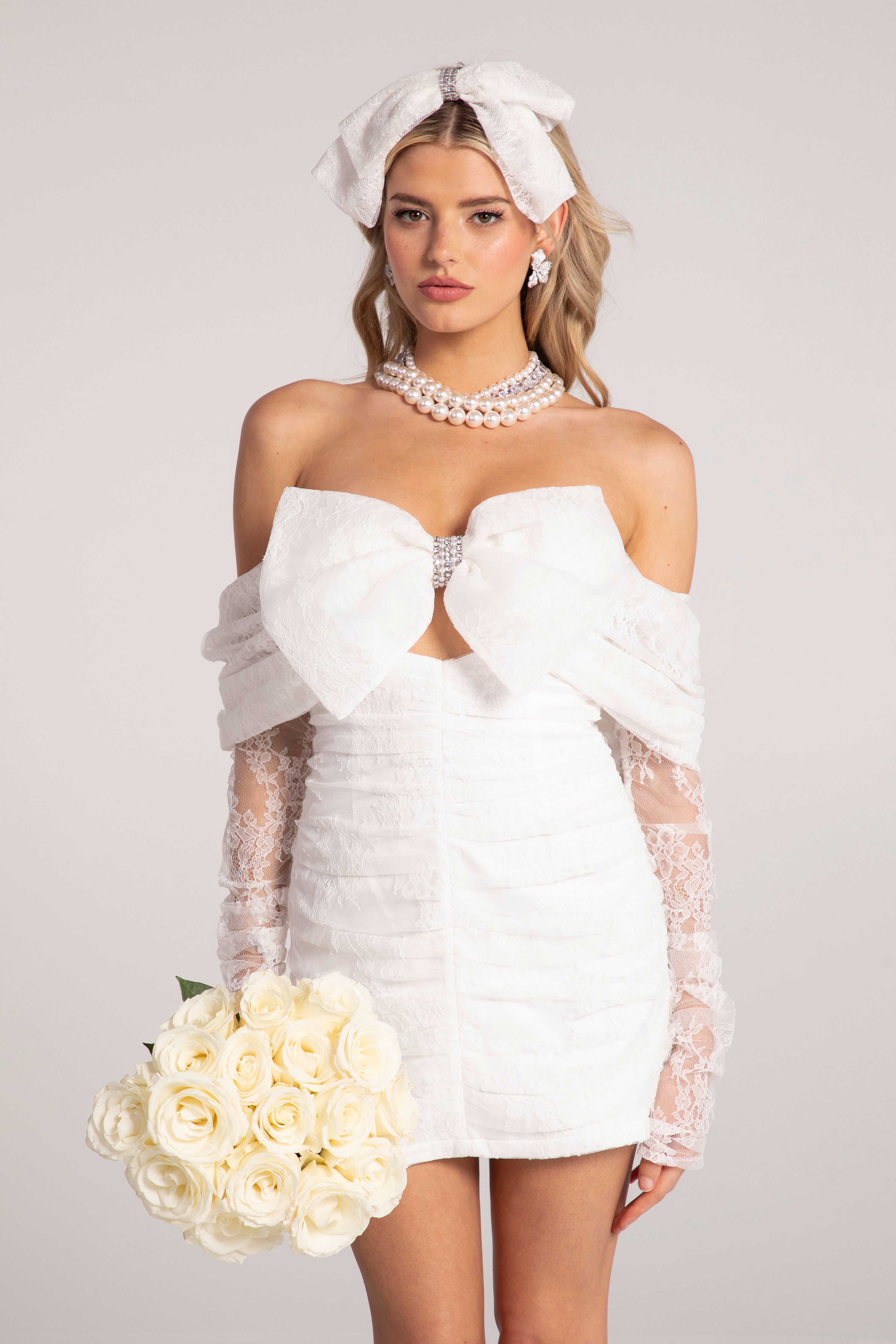 Woman in a white wedding dress with gloves and a bouquet on a plain background