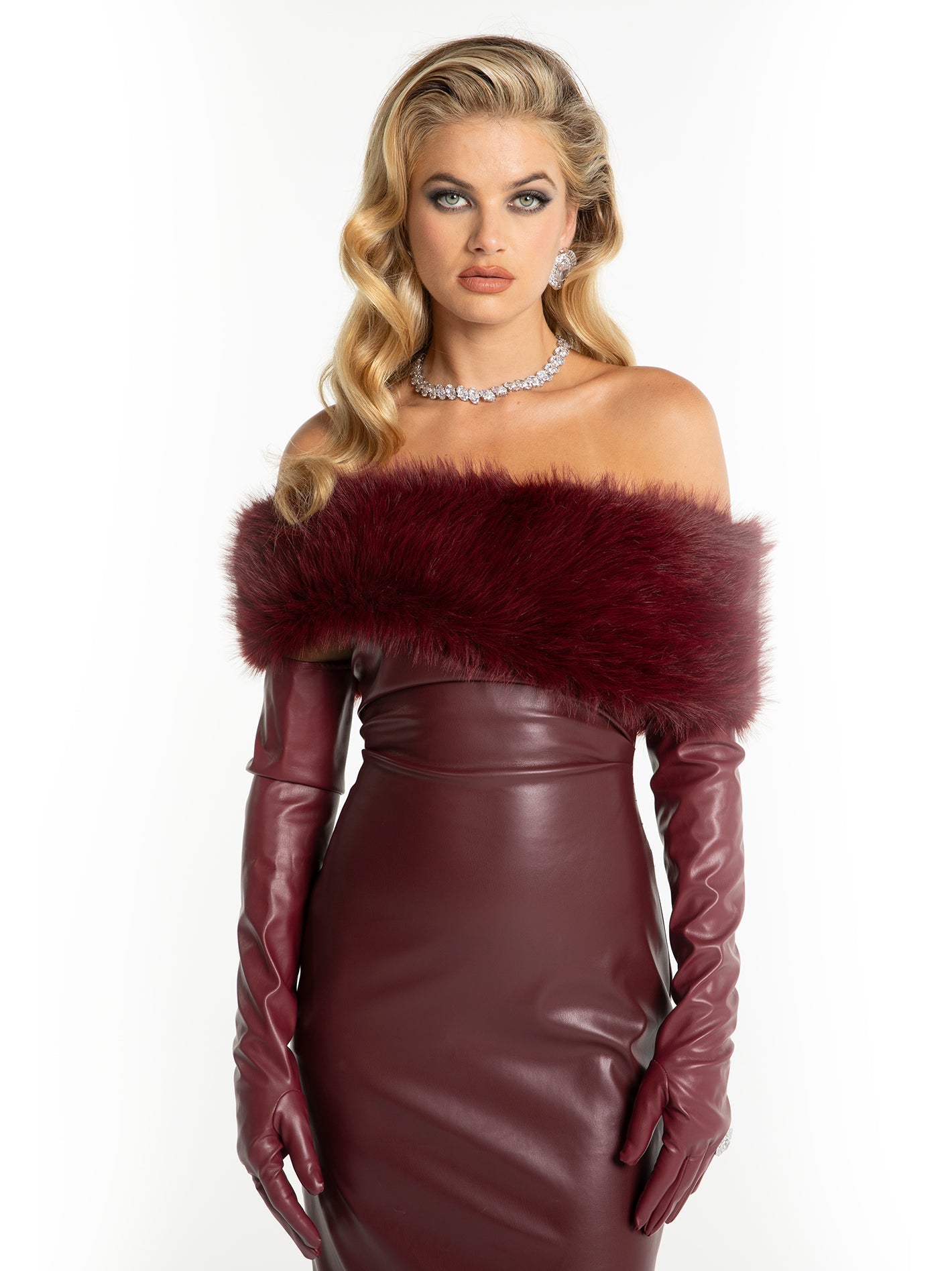 Woman wearing a burgundy leather dress with fur trim and matching gloves on a white background