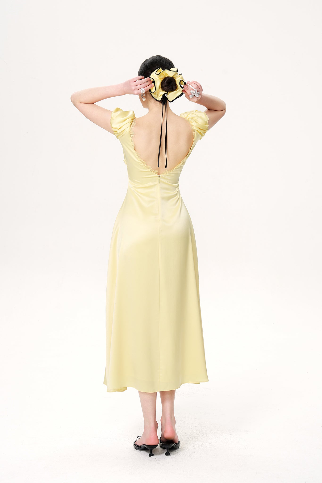 Woman wearing a yellow dress with a black hat and shoes on a white background