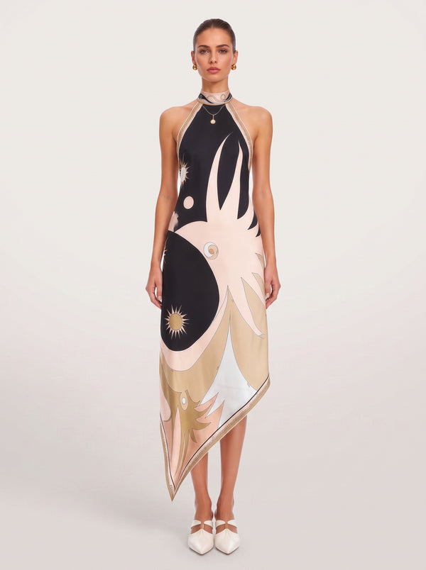 A model wears a sleeveless halter-neck midi dress featuring an abstract yin-yang style print in black, beige, and white, paired with white pointed-toe flats against a light gray studio background.