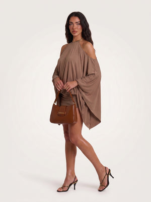 A woman modeling a draped, cold-shoulder taupe-brown mini dress with a matching handbag and strappy heels against a light off-white studio background.